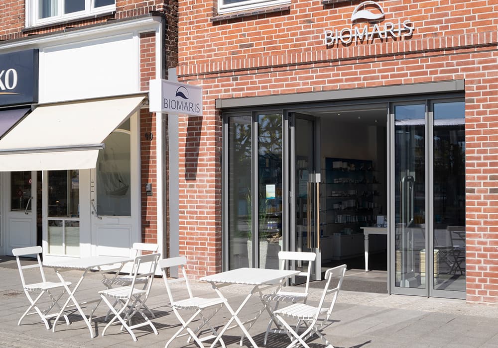 BIOMARIS Shop Eingangsbereich mit Glasfront und weißen Bistrostühlen vor dem Geschäft in rotem Ziegelbau