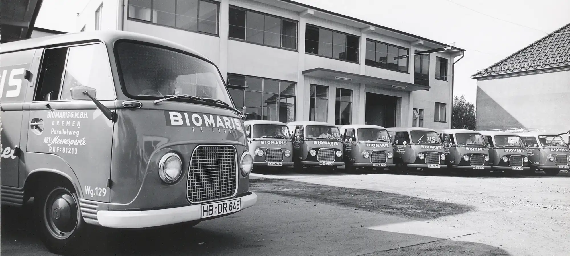 Historische Aufnahme mit mehreren BIOMARIS Lieferwagen vor einem Firmengebäude
