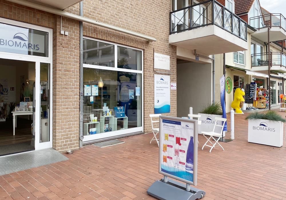 Eingang des BIOMARIS Shops Scharbeutz mit Werbetafel und Sitzgelegenheit auf rotem Pflaster in Einkaufsstraße