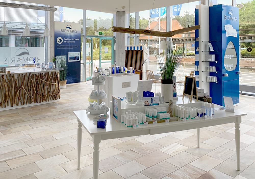 Innenansicht des BIOMARIS Shops mit Produkten auf weißen Tischen, hellem Boden und dekorativer Theke im maritimen Stil