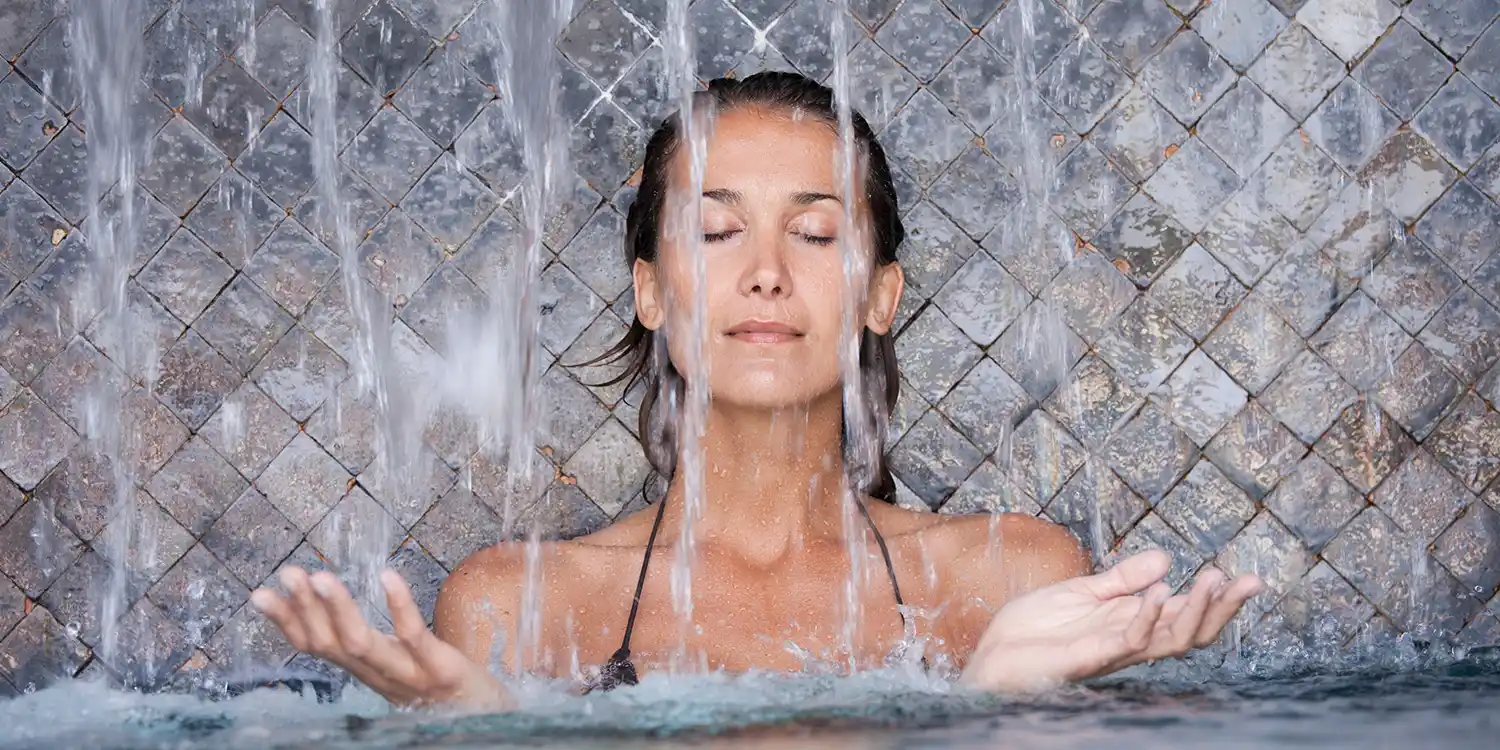  Frau mit geschlossenen Augen unter Wasserstrahlen in einem Spa-Becken