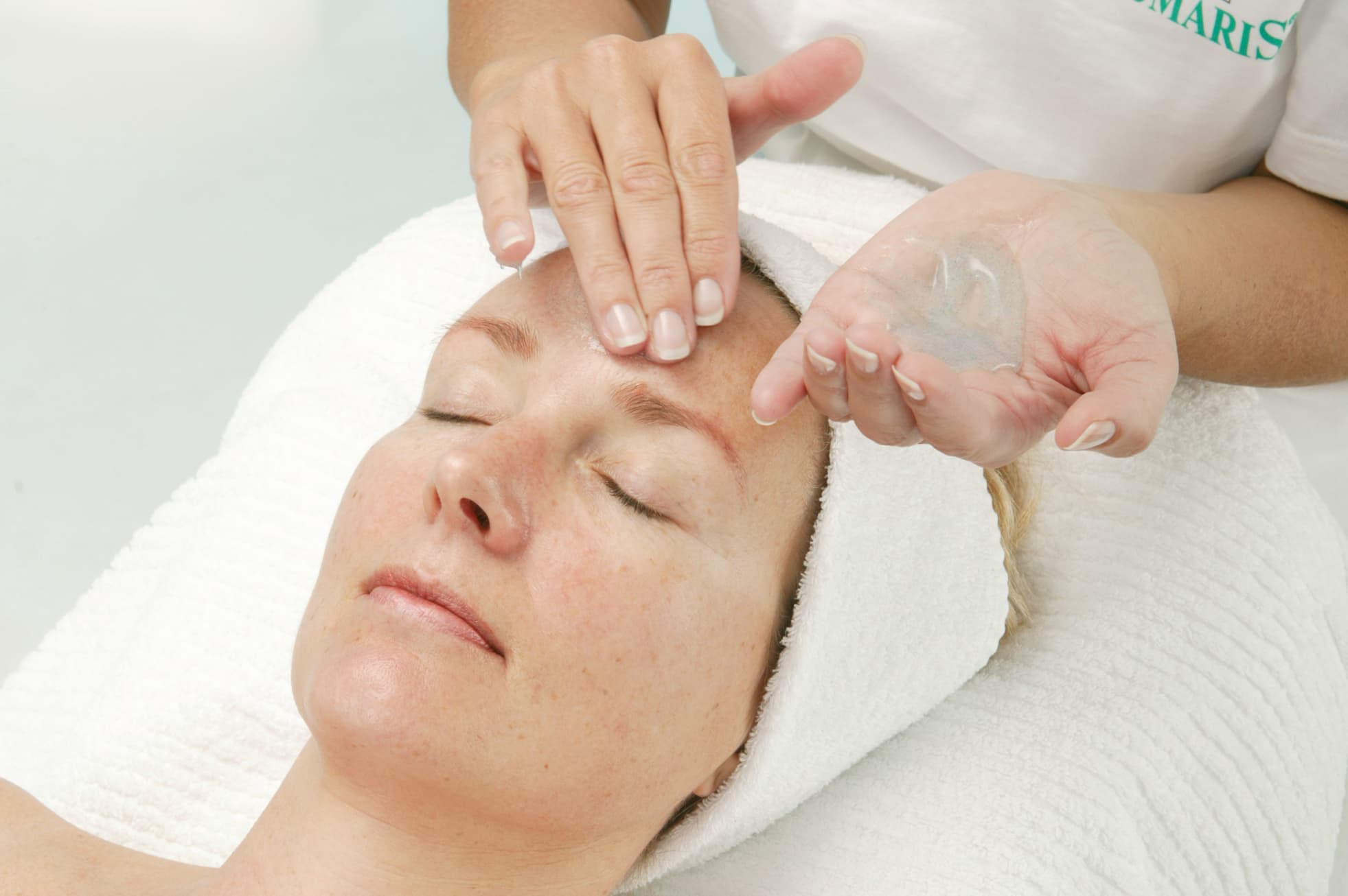Frau mit geschlossenen Augen erhält eine sanfte Gesichtsmassage mit Gel durch eine Kosmetikerin in einem Kosmetikinstitut.